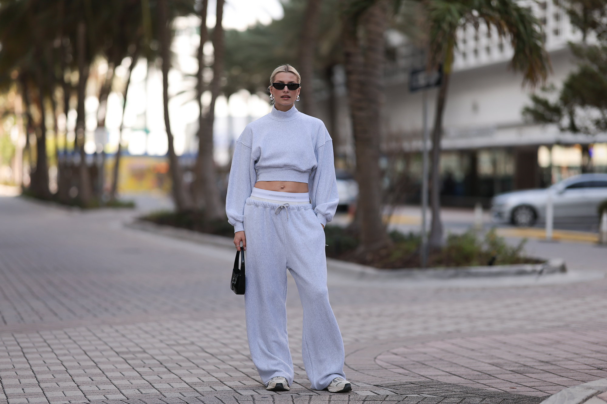 MIAMI, FLORIDA - DECEMBER 08: Lena Gercke seen wearing Saint Laurent black sunglasses, silver statement necklace, Alexander Wang light grey high neck cotton cropped jumper / sweater, Alexander Wang light grey cotton wide leg jogger pants with underwear detail, Saint Laurent black varnishes leather mini bag and Axel Arigato white leather sneakers, on December 08, 2023 in Miami, Florida. (Photo by Jeremy Moeller/Getty Images)2