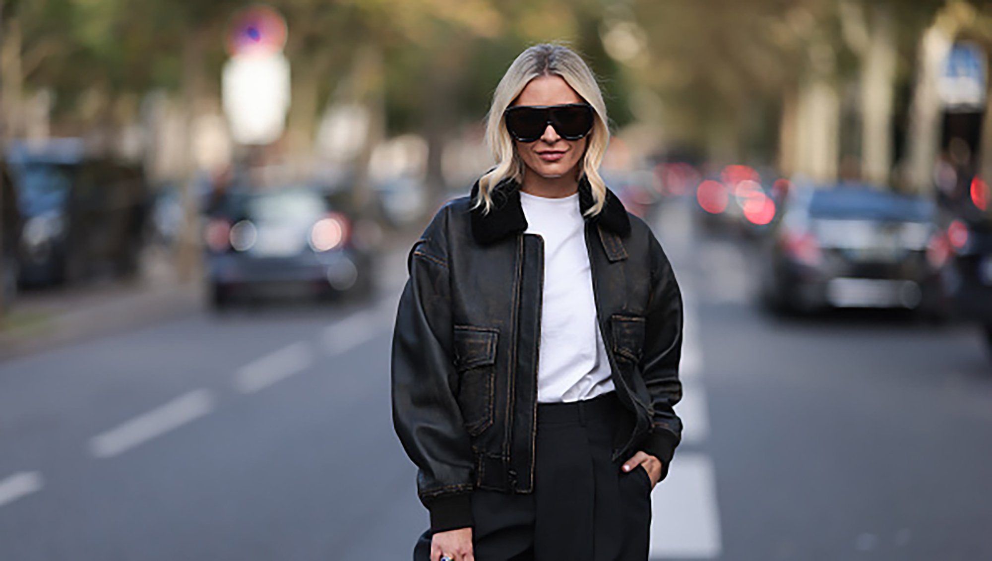 PARIS, FRANCE - SEPTEMBER 29: A Fashion Week guest is seen wearing large black shield-frame sunglasses, a distressed dark brown leather jacket with fluffy black collar, a white top tucked into black suit pants, a chunky gold ring with blue stone, and a beige suede “Birkin“ bag from Hermès before the Atlein Womenswear Spring/Summer 2025 Show as part of Paris Fashion Week on September 29, 2024 in Paris, France. (Photo by Jeremy Moeller/Getty Images)